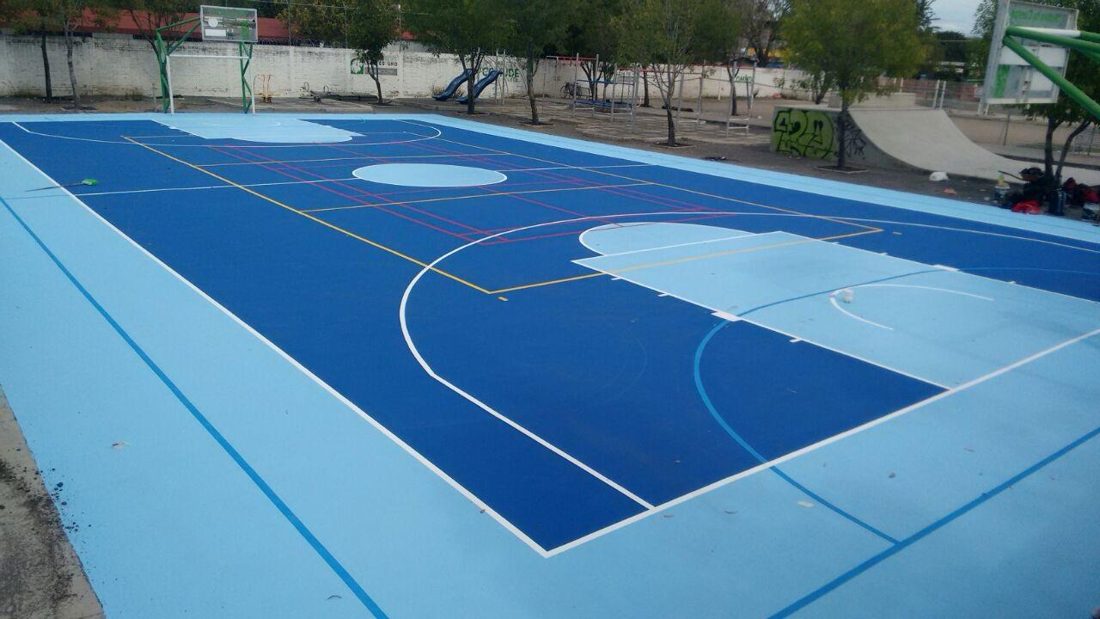 Cancha de usos múltiples con superficie acrílica en dos tonos de azul, en un parque con rampa de skate