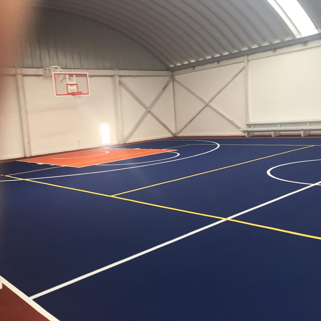 Cancha de básquetbol acrílica azul marino bajo un techo de lámina, con líneas blancas y amarillas