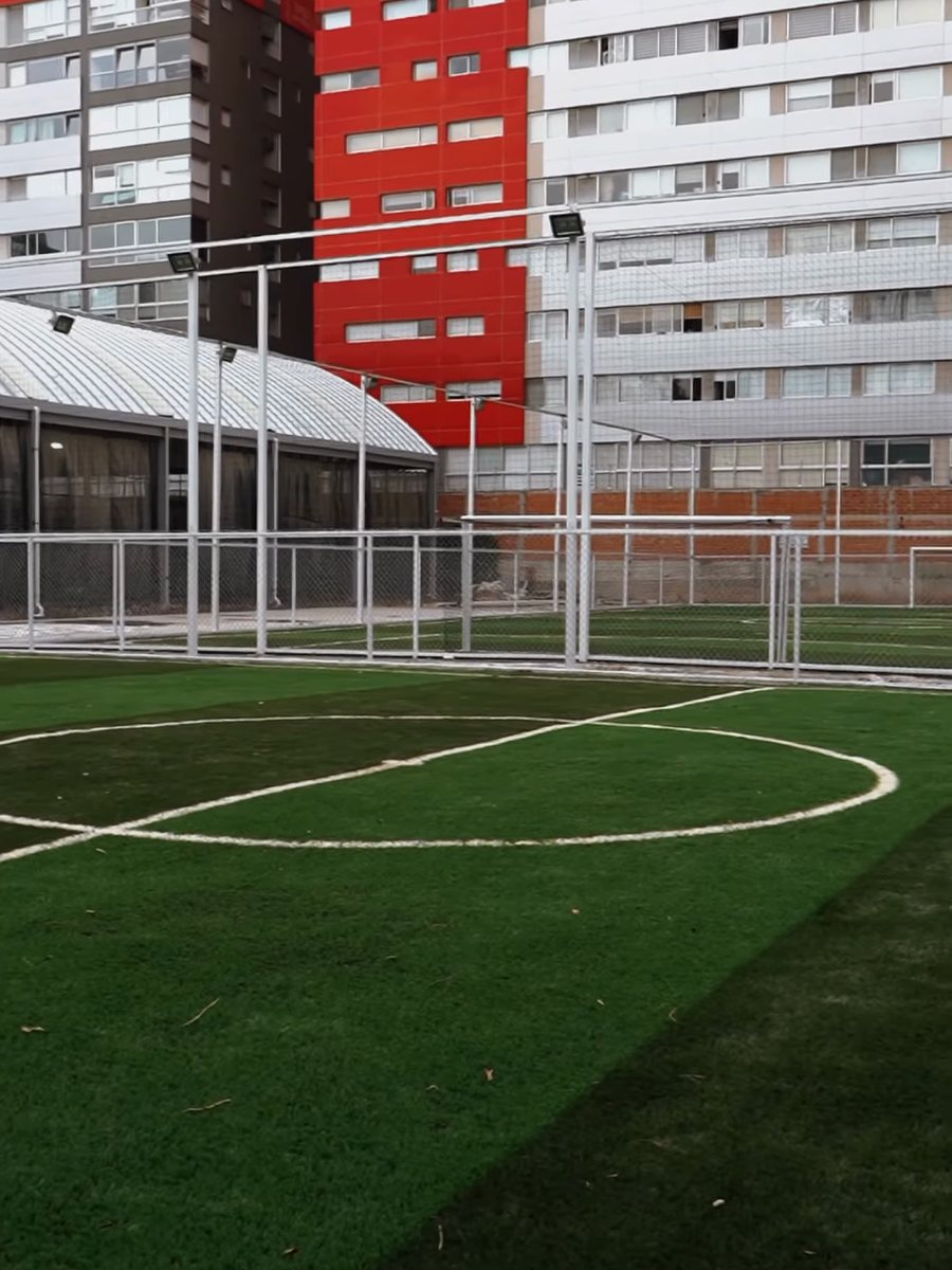 Cancha de fútbol de pasto sintético entre edificios, uno de ellos rojo