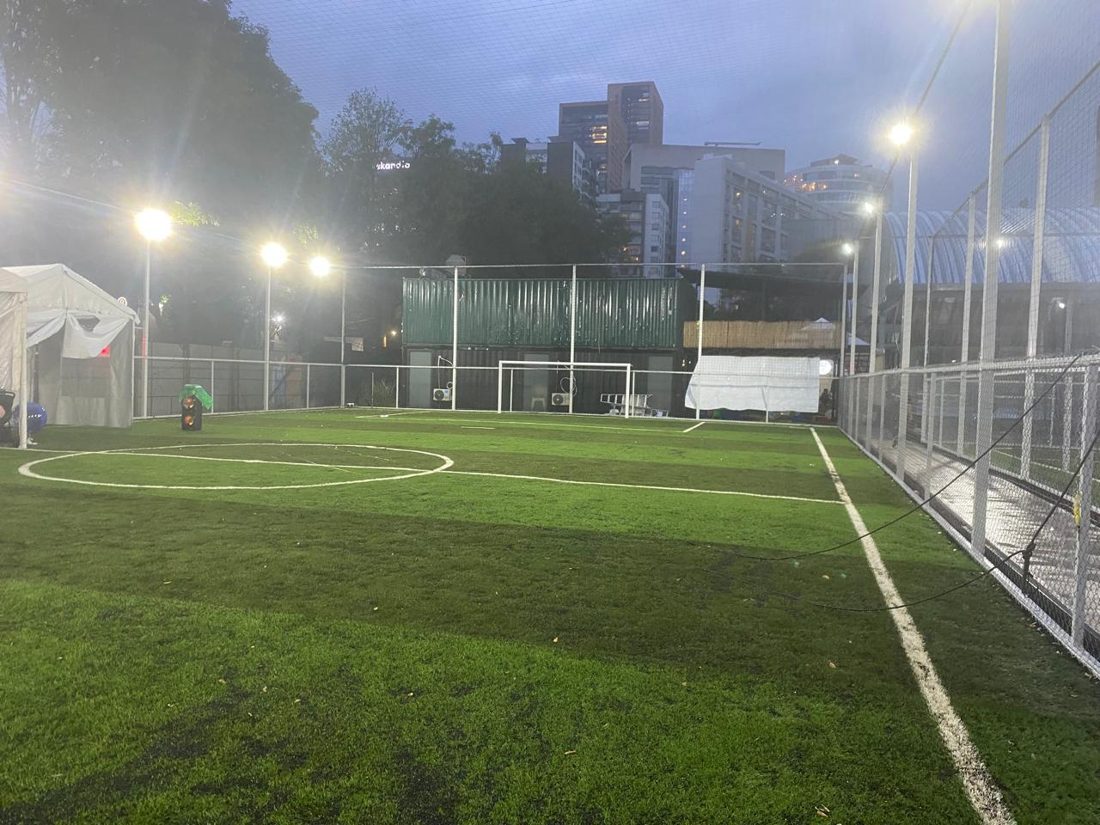 Cancha de fútbol de pasto sintético de noche, con reflectores encendidos alrededor