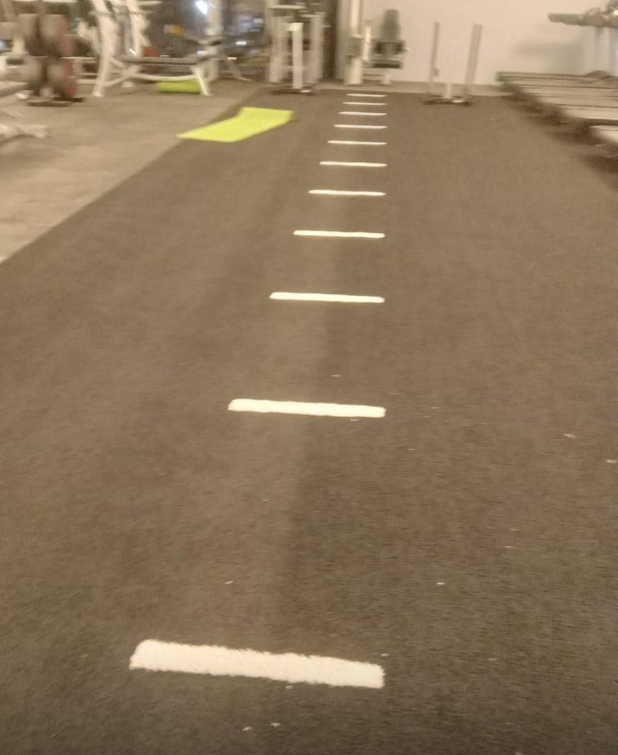 Carril de pasto sintético gris en un gimnasio, con marcas blancas a lo largo
