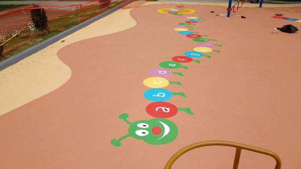 Piso de hule color salmón con una oruga del abecedario pintada en un área de juegos