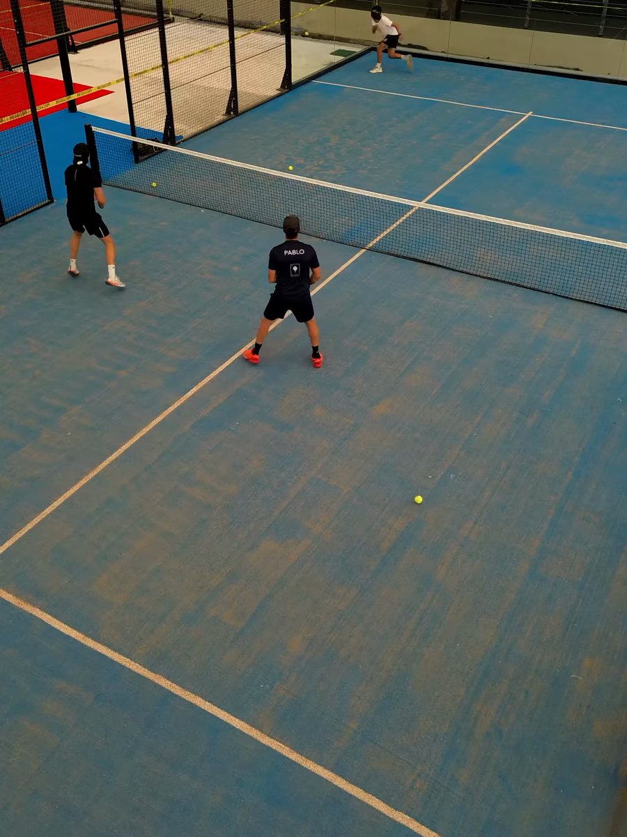 Dos jugadores en una cancha de pádel de pasto azul, bajo techo