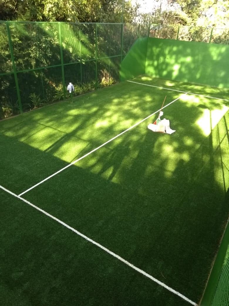Cancha de pádel de pasto verde entre árboles, con muros pintados de verde