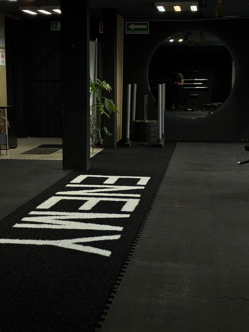 Pista de pasto sintético negro con letras blancas incrustadas, en un gimnasio