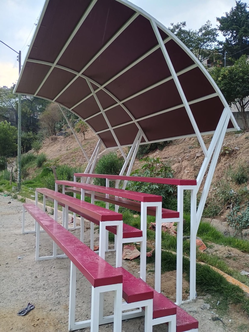 Gradas de herrería blancas y rojas con techo curvo, sobre un talud