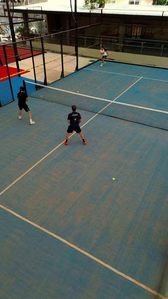 Complejo de pádel techado con domo blanco y canchas azul y roja, con gente jugando
